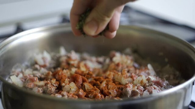 Hand adding spices to a mix of meat and onions to be used in empanadas while they are being cooked. Slow motion (120fps)