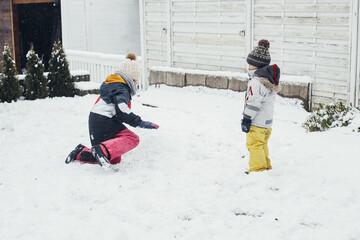 Children, brother and sister play in the backyard of their house in the snow. Winter, winter fun, family walks