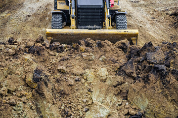 Tractor with with backhoe for earthmoving works in construction site pit. Front view. Moving soil in the pit.