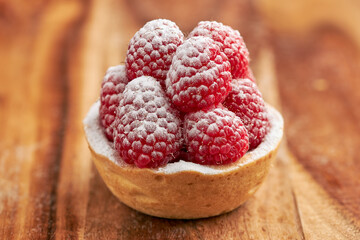 Appetizing raspberry tart with icing sugar on a sponge cake base on a wooden table. - obrazy, fototapety, plakaty