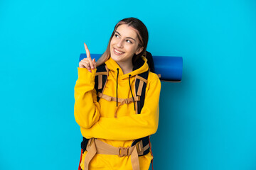 Young mountaineer woman with a big backpack isolated on blue background pointing up a great idea