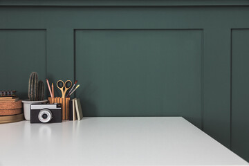 Desk at home office with supplies and dark green wall copy space. Minimalistic workspace.	
