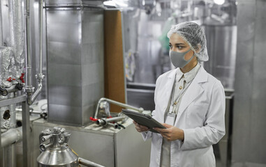 Waist up portrait of female worker wearing mask and holding digital tablet during quality control inspection at food factory, copy space
