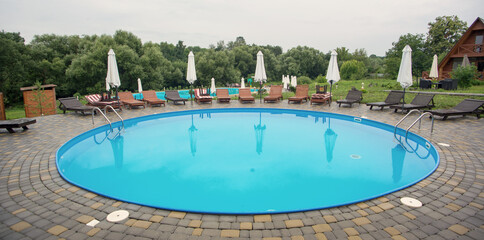 The round swimming pool with wooden deckchairs and umbrellas.