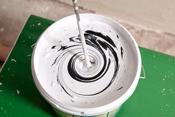 House painter mixes black and white paint to get a gray color using an electric drill and paddle...