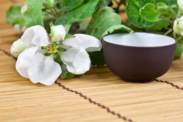 Obraz na płótnie Canvas Green tea in a ceramic cup with branches of blossoming apple tree on a bamboo background. Spring background.