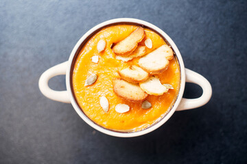 pumpkin cream soup with croutons on a black table with spices