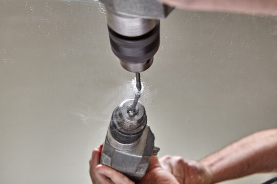 Worker drills hole in surface of mirror using glass drill bit.
