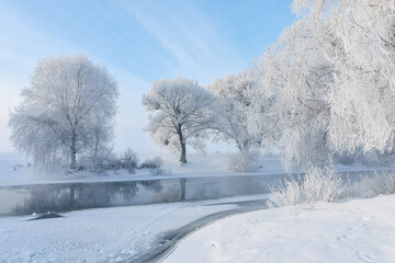 Idyllic snowy winter landscape panorama with trees, river, heavy hoarfrost and sun. Winter sunrise,...