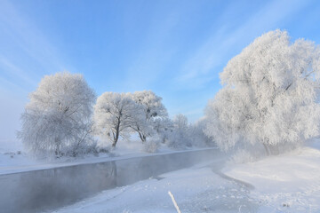 Idyllic snowy winter landscape panorama with trees, river, heavy hoarfrost and sun. Winter sunrise,...
