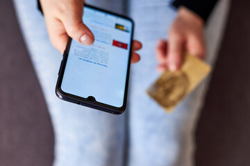 A woman makes purchases on the Internet using a smartphone and her bank card.
