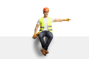 Construction worker with a helmet sitting on a blank panel and pointing to the side