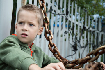 Boy in a green sweater holds a rusty chain
