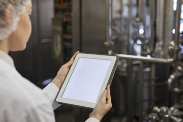 Close up of young female worker holding digital tablet with blank white screen against factory...