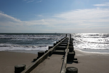 Coastal landscape showing the sandy beach, rough ocean and wooden jetty extending into the ocean