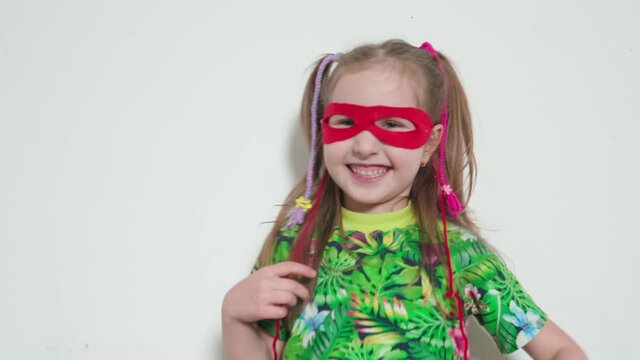 a little girl puts a red mask on her face, she is a super hero. baby girl jumps and has fun. children's fantasy games. happy child dancing and enjoying life