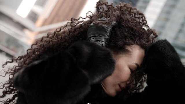 Portrait of a curly-haired woman in a fur coat posing against the background of a winter city, enjoying a beautiful day. The carefree lady is set against a backdrop of beautiful buildings.