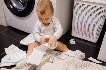 Infant or toddler baby tearing toilet paper and eat it. There are a lot of rolls on the floor....