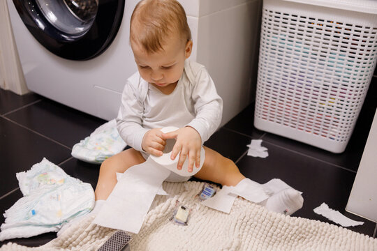 Infant Or Toddler Baby Tearing Toilet Paper And Eat It. There Are A Lot Of Rolls On The Floor. Close-up