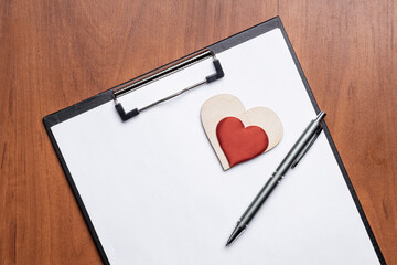 blank clipboard over wooden desk, decorated heart symbol. above view. valentine goals card template. love contract conceptual