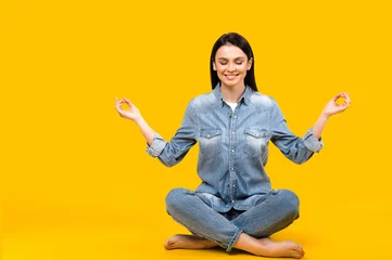 Fotobehang Keep calm. Photo of a satisfied calm caucasian young woman with closed eyes, meditates in lotus position on isolated white background © Kateryna
