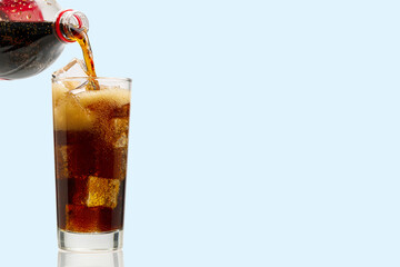 Pouring Cola to glass with ice cubes isolated on blue