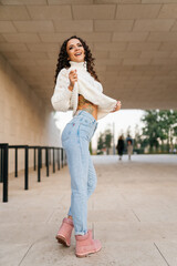 Slender beautiful brunette in blue jeans dances slightly lifting the edge of a white sweater. High quality photo
