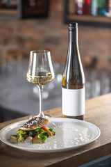 Healthy fish cooked with steamed vegetables served on a plate next to a bottle of white wine