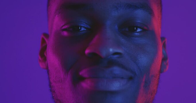 Close up portrait of african american man looking at camera in neon light and smiling