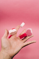 A hand throwing some little hearts of sponge with different colors on a pink background. The hearts are dispersed on the hand. San Valentine's day backgrounds concept