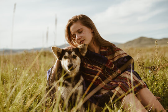 in the steppe against the backdrop of hills on the grass sit a girl and her dog. the girl is wrapped in a shawl and covered her eyes cuddling up to an eared friend. High quality photo