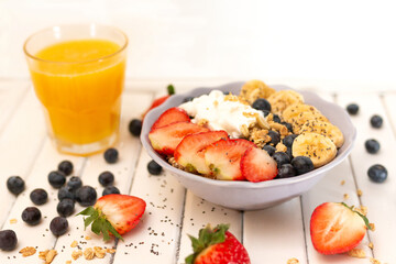 Breakfast bowl with granola and with fresh berries, banana, orange jouce served on white wooden  background 