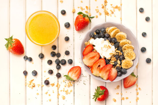 Breakfast bowl with granola and with fresh berries, banana, orange jouce served on white wooden  background. 