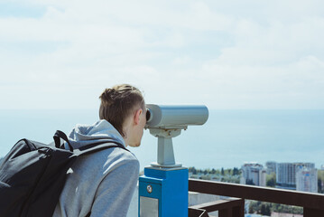 Fototapeta na wymiar young hipster tourist man looking through metal coin operated binoculars on sea, sky and city, horizontal lifestyle stock photo image