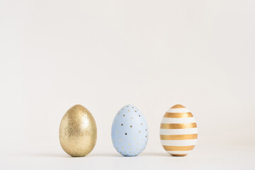 Three Easter golden decorated eggs on white background. Minimal easter concept. Happy Easter card with copy space for text. Top view, flatlay.
