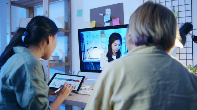 Asia businesswomen using desktop talk to colleagues about plan in video call meeting at living room. Working from house overload at night, remotely work, social distancing, quarantine for coronavirus.