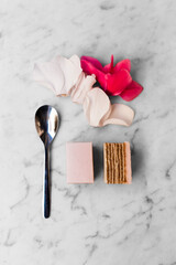 Pink cake, a spoon and flower petal decoration on white marble background.
