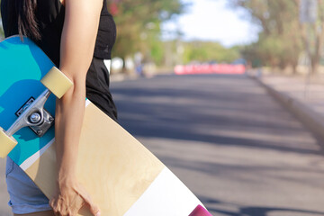 Close up on young women hand hold skateboard, surf skate on public park background. Free relax skateboard trendy concept. Fashion portrait of female hands holding surf skateboard