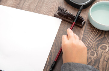 The calligrapher is about to pick up the brush on the holder and the inkstone and brush washer beside it