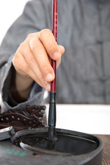 The calligrapher sticks ink in the inkstone with a brush in his hand