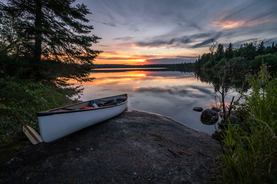 A canoe stopped on shore at sunset on a calm and peaceful lake in Northwest Ontario, Canada.