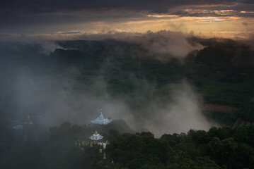 White Buddhist pagoda complex on a hill top in a green forest at sunrise time