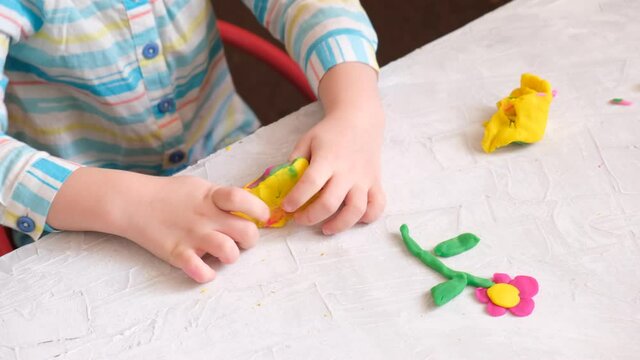Hands of little girl making flower  and other shapes from colorful clay dough, plasticine, with unexpected outcome of ending. Home Education game with clay. Early development concept