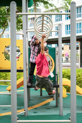 Young asian children hang on the monkey bar. To exercise at outdoor playground in the neighbourhood.