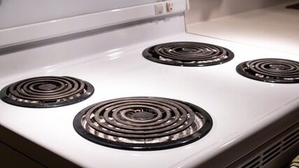 Stovetop burners on a white stove, dimly lit, Toronto, Canada. 