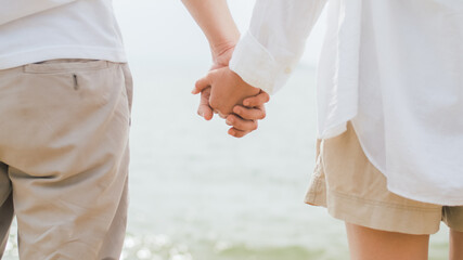 Close up couple hold hands while standing on the beach on holiday summer, Asian loving couple holding hands on a beach near the sea.