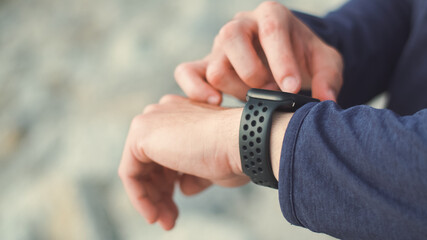 Close up hands tired sportsman wearing sportswear standing outdoors resting after a workout and using the smartwatch checking heart rate.