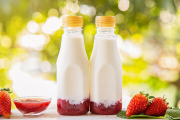 Homemade strawberry milk in a bottle on white wooden table with strawberry fruits with nature background