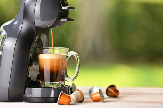 Coffee machine making coffee with capsules on wooden table