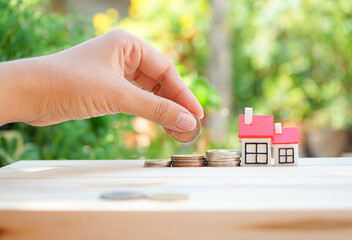 Hand holding coin with miniature house in concept of saving money for buying home, real estate or financial
